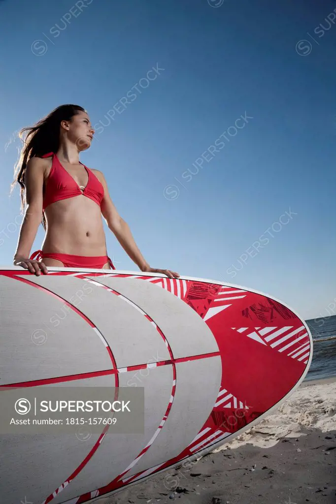 Germany, St Peter-Ording, young woman with stand up paddling surfboard at beach