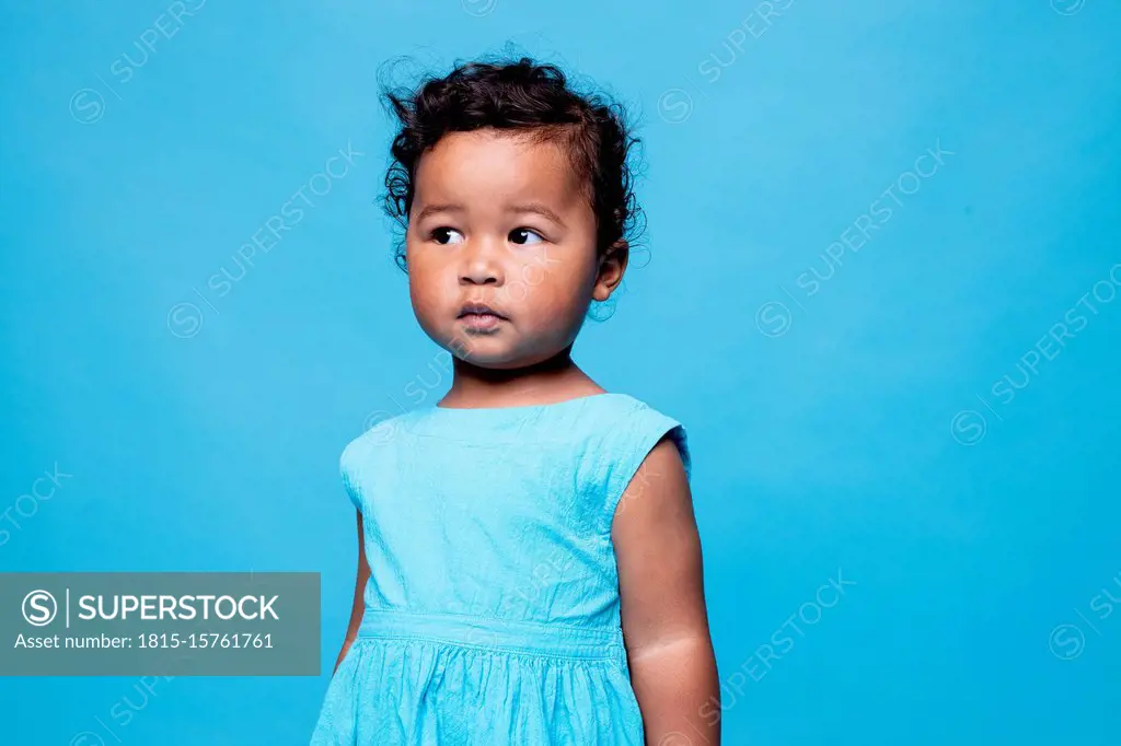 Portrait of little girl wearing light blue dress against blue background