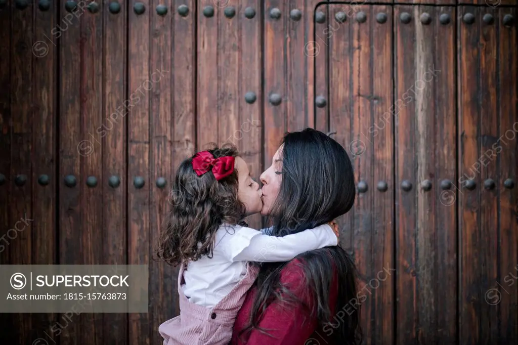 Mother holding and kissing little daughter outdoors