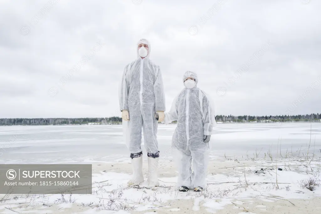 Father and son wearing protective suits standing at frozen river