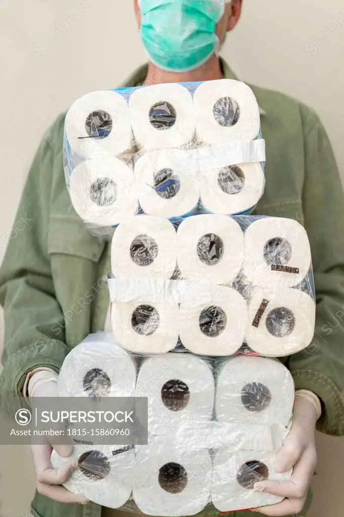 Man with face mask and protective gloves, holding packets of toilet paper