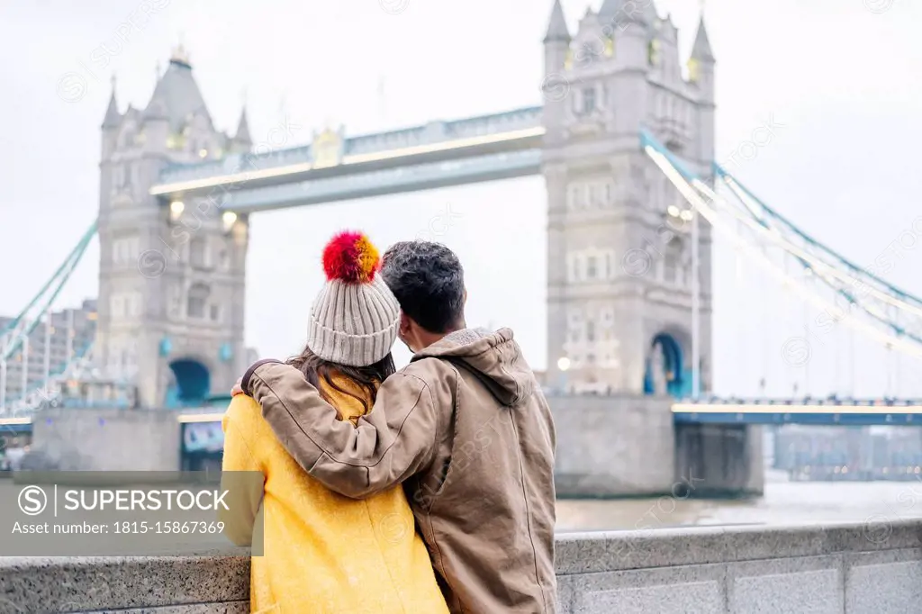 Two young tourists sitting on wall, using smartphone, with London Bridge in background