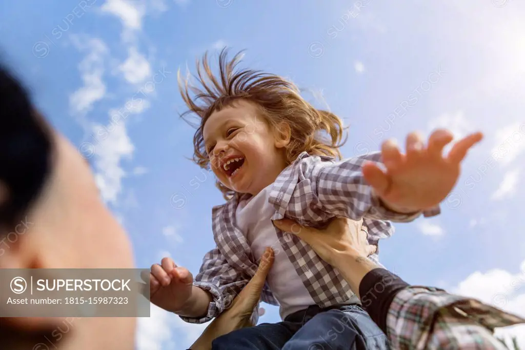 Mother lifting up happy toddler son outdoors