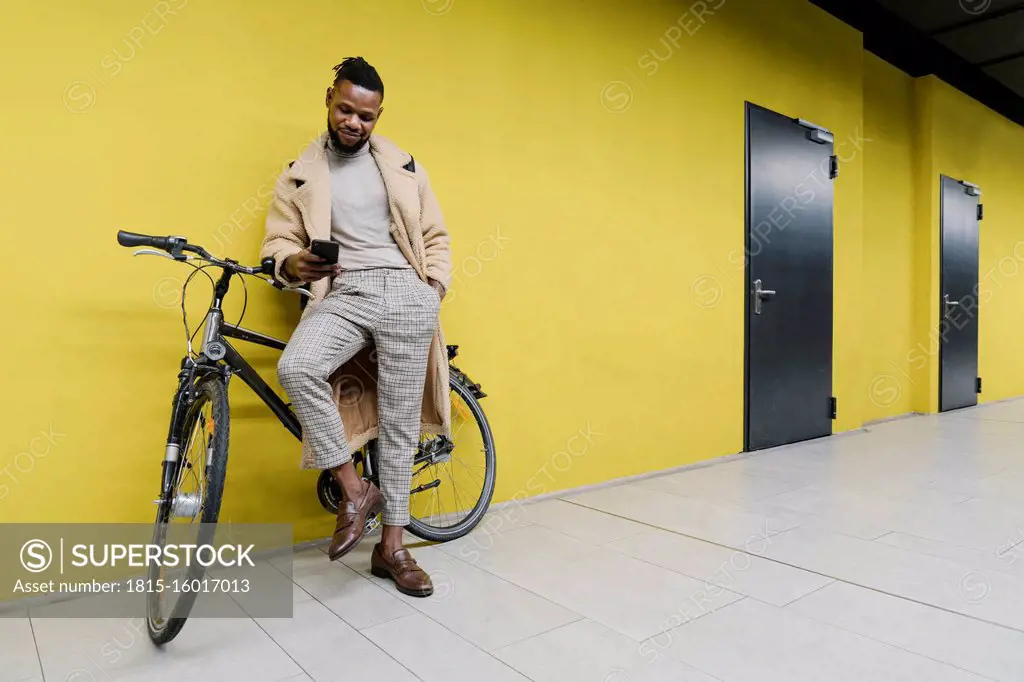 Stylish man with a bicycle and smartphone at a yellow wall