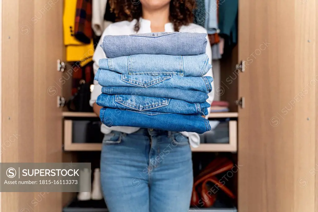 Woman standing on front of wardrobe holding stack of blue jeans