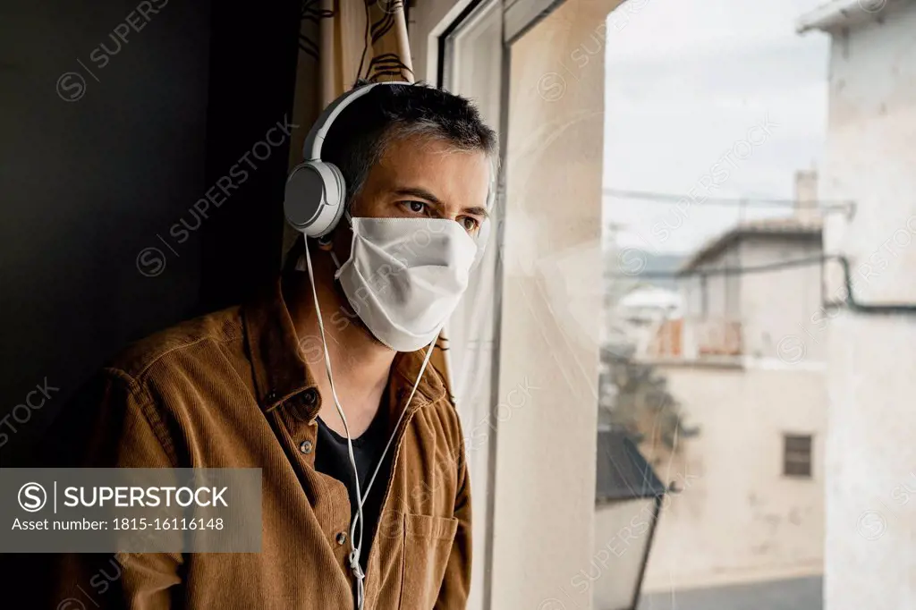 Man wearing protective mask and white headphones looking out of the window