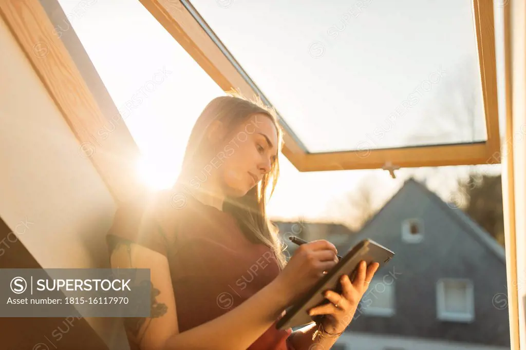 Young woman using graphics tablet at the window in backlight