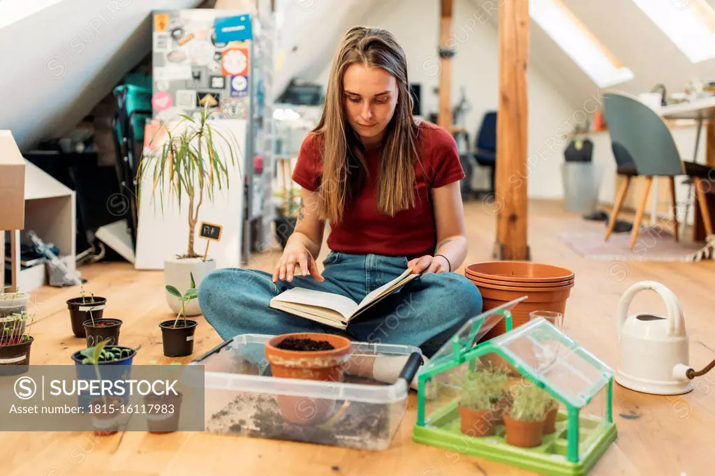 Young woman ureading book next to plants on wooden floor