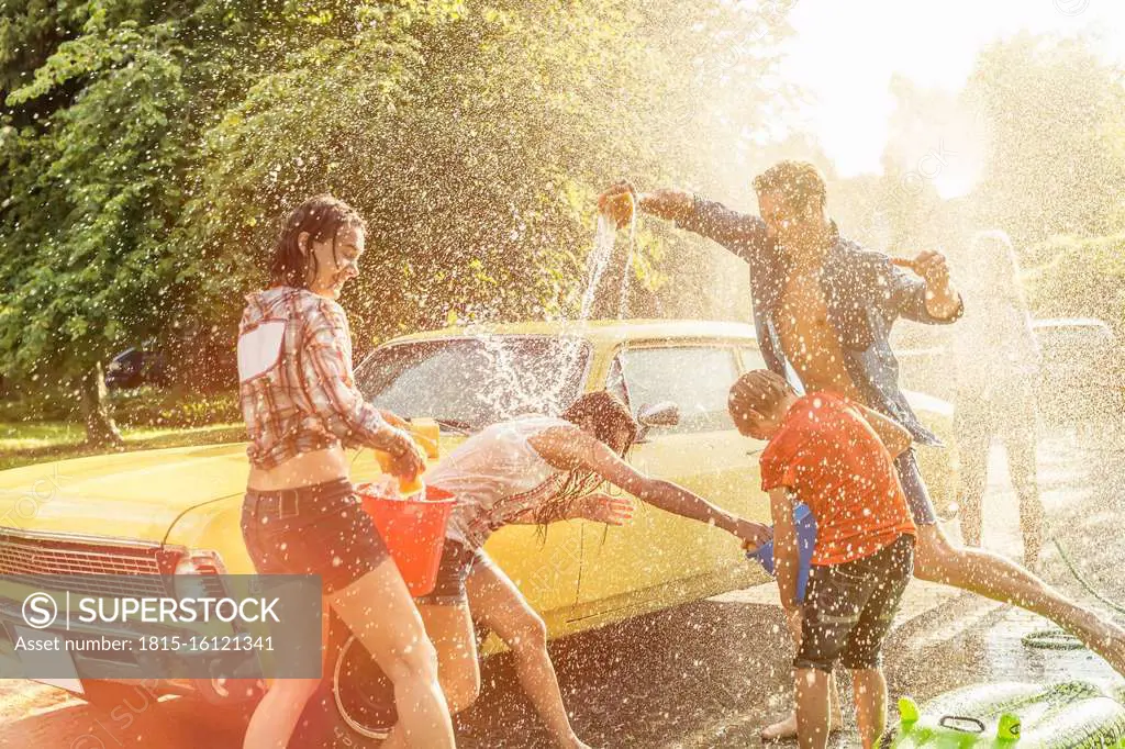 Group of friends washing yellow vintage car in summer having fun