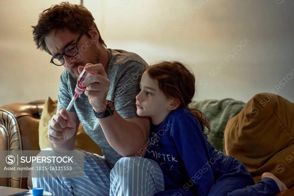 Sick girl looking at father preparing medicine for her while sitting in living room at home