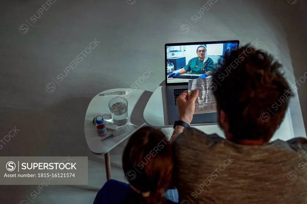 High angle view of family discussing telemedicine with doctor over video call through laptop in living room at home