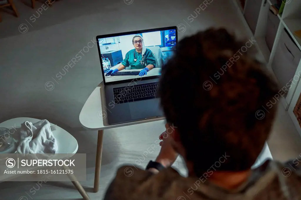 Rear view of man consulting doctor over laptop in living room at home