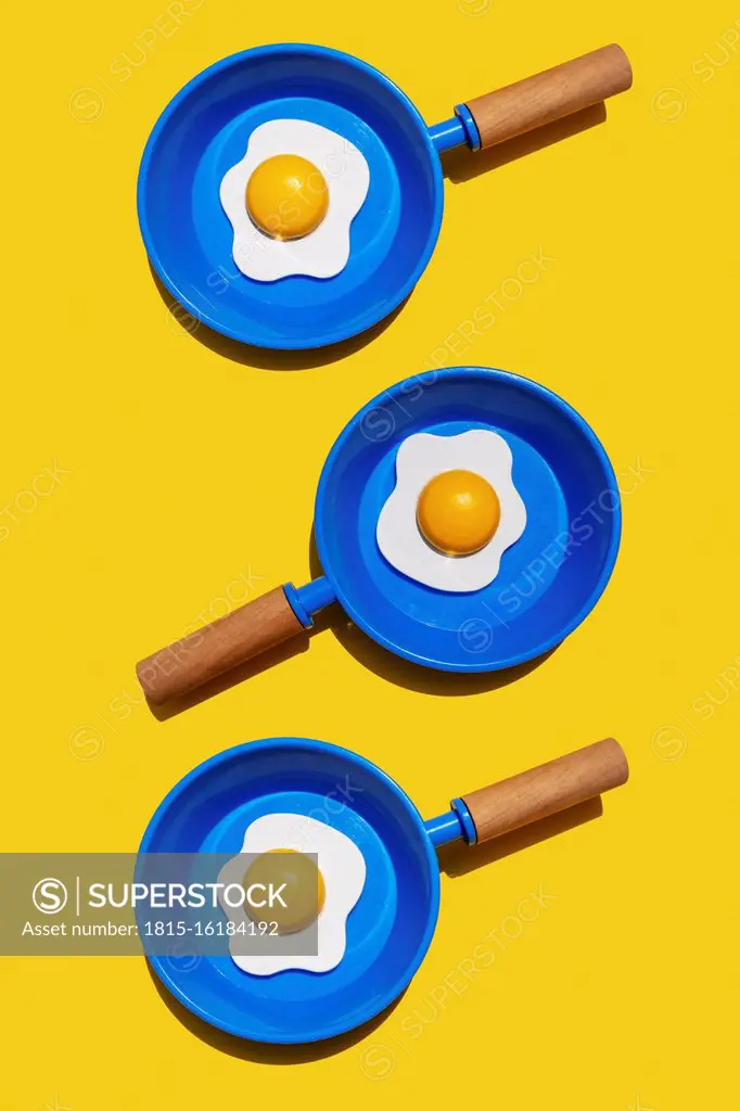Illustration of fried eggs on blue pans against yellow background