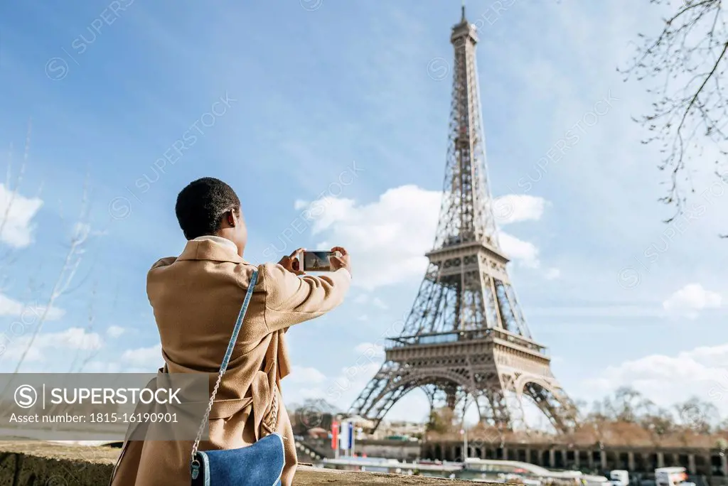 Woman photographing Eiffel Tower through smart phone against sky, Paris, France