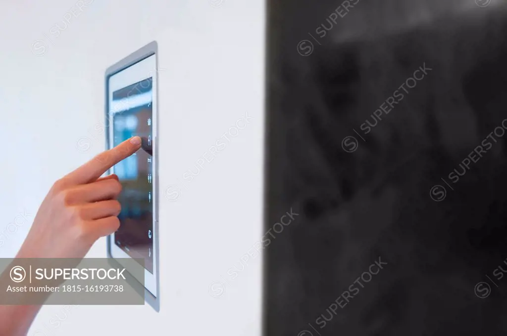 Hand of woman using digital lightning control mounted on wall at home