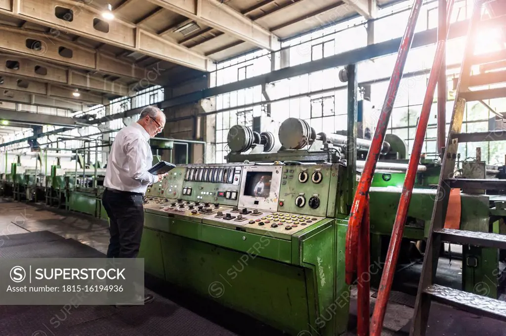 Senior businessman examining a machine in a factory hall