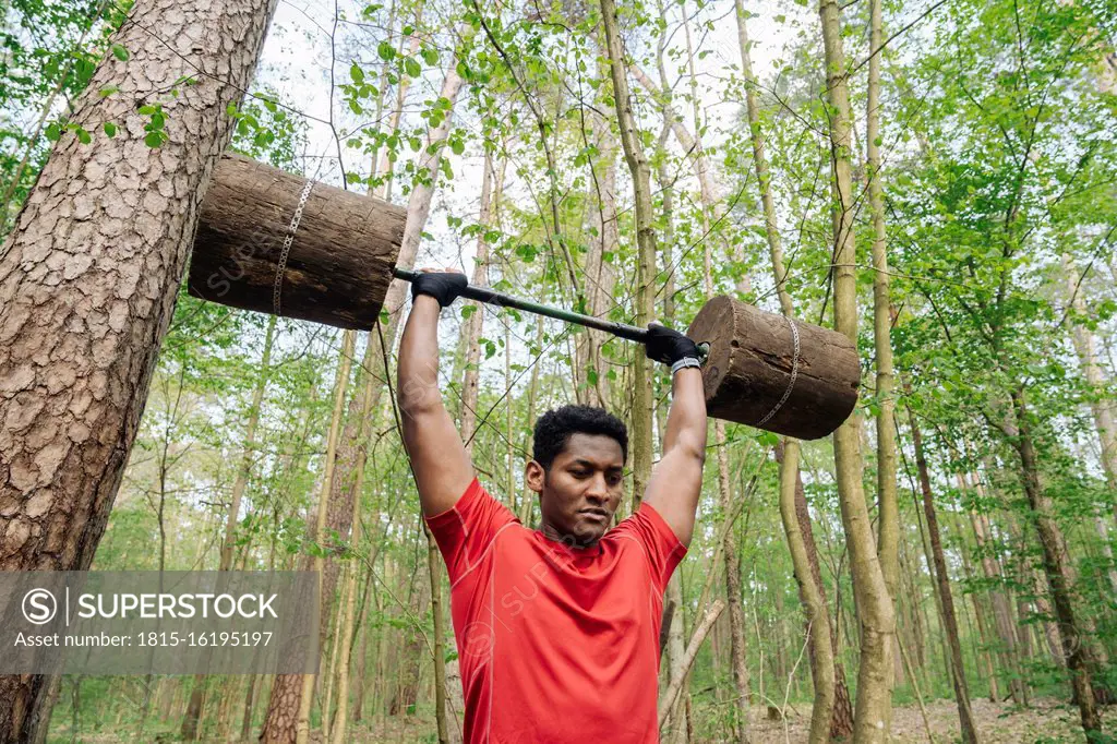 Sportsman exercising with wooden barbells in the forest