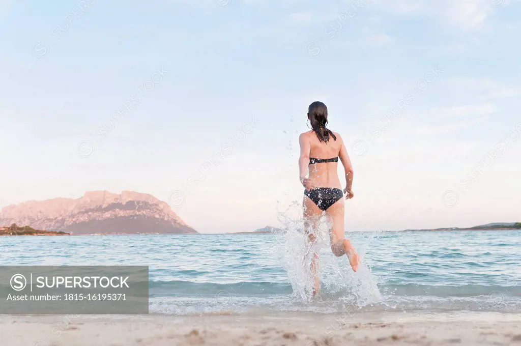 Back view of woman in bikini running into the sea, Sardinia, Italy