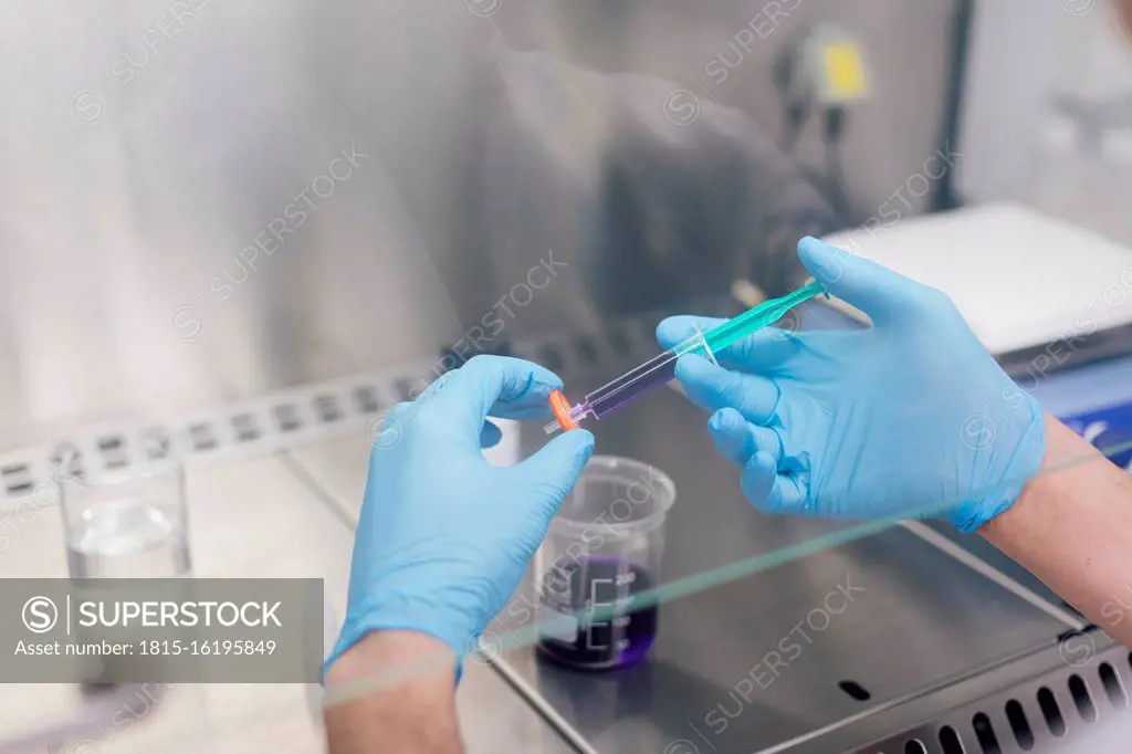 Hands of male technician holding syringe with chemical over beaker in lab