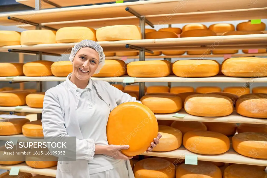 Cheese factory, smiling female worker holding cheese wheel