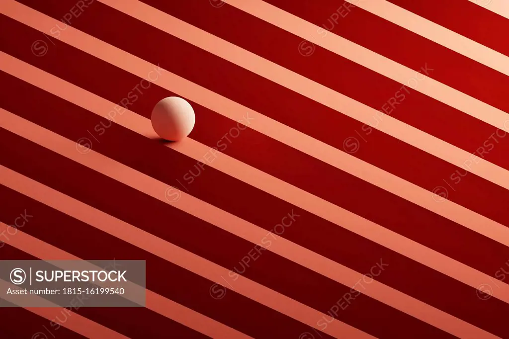 Three dimensional render of small light brown sphere rolling over geometric pattern