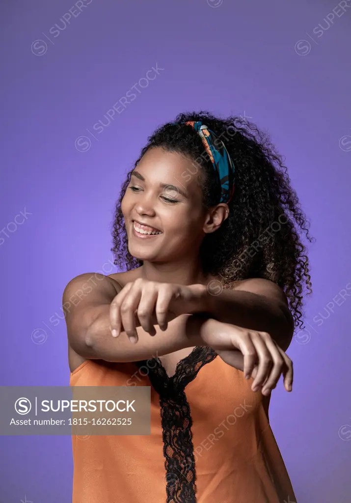 Cheerful young woman with curly hair dancing against purple background