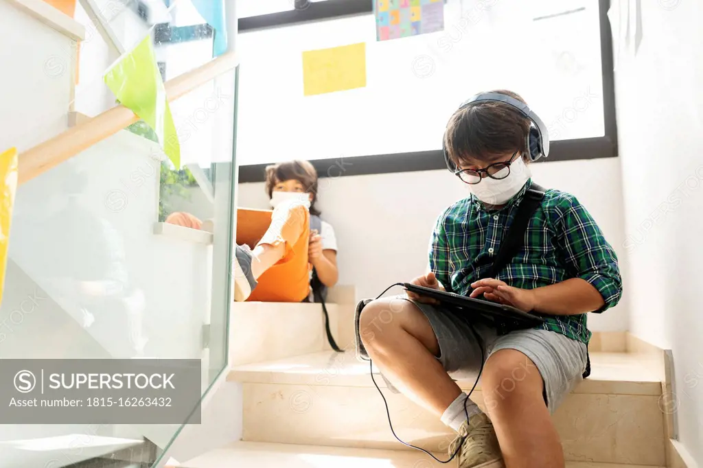 Boys wearing masks studying while sitting at distance on steps in school