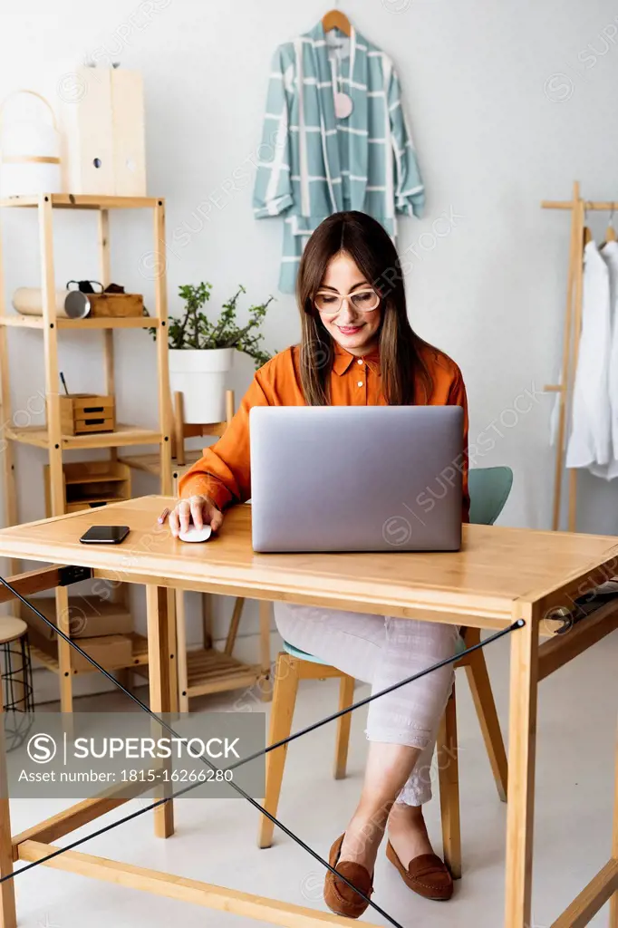 Female fashion designer working at home sitting at desk with laptop