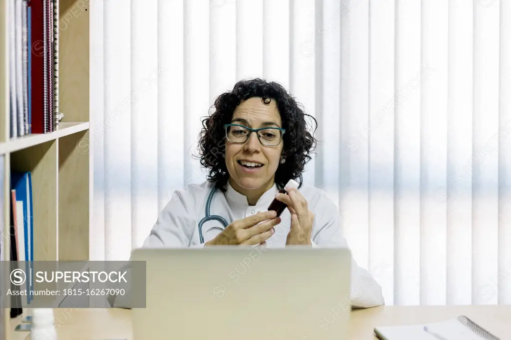Smiling female doctor discussing medicine through video call on laptop in office