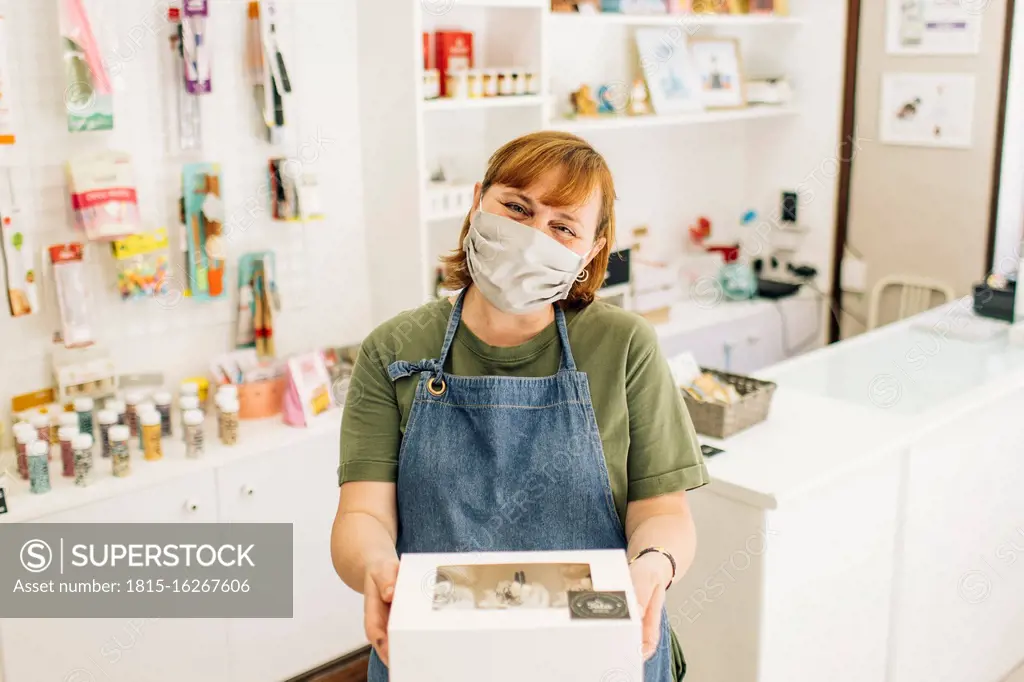 Female baker wearing mask delivering cupcake box while standing in store