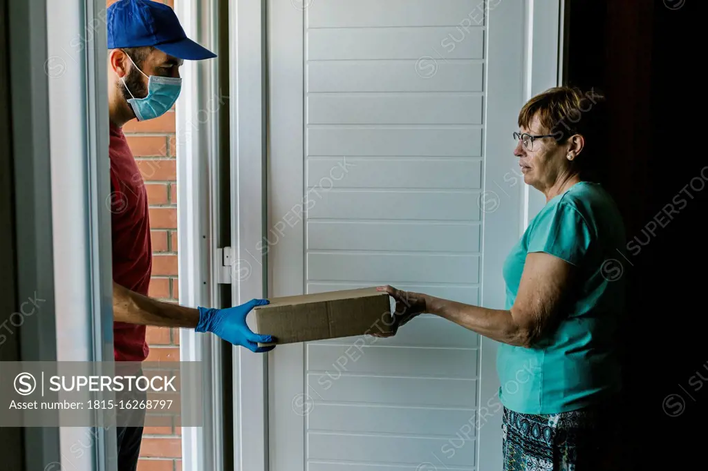 Postal worker delivering package to senior woman at doorway during coronavirus