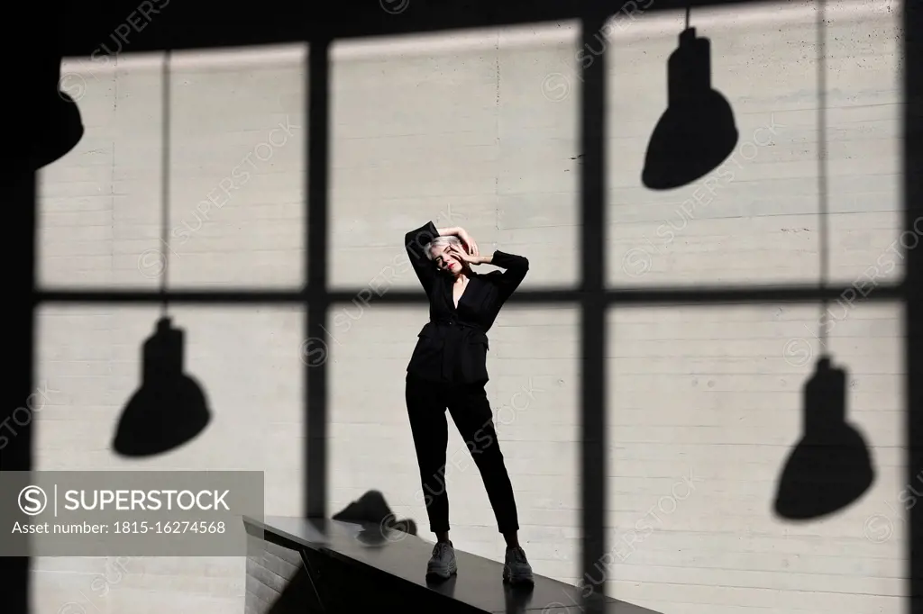 Stylish businesswoman wearing suit standing on retaining wall with sunlight and shadow in background