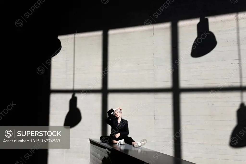 Female professional wearing elegant suit relaxing on retaining wall with sunlight and shadow in background