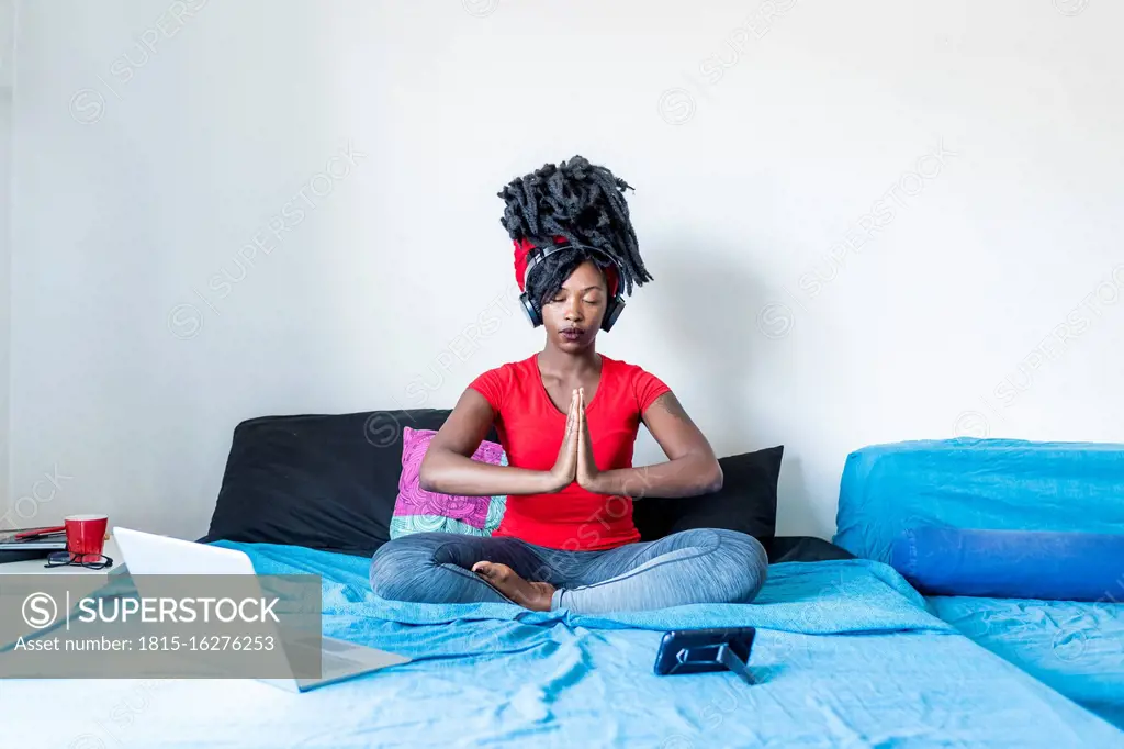 Young woman meditating at laptop sitting on bed
