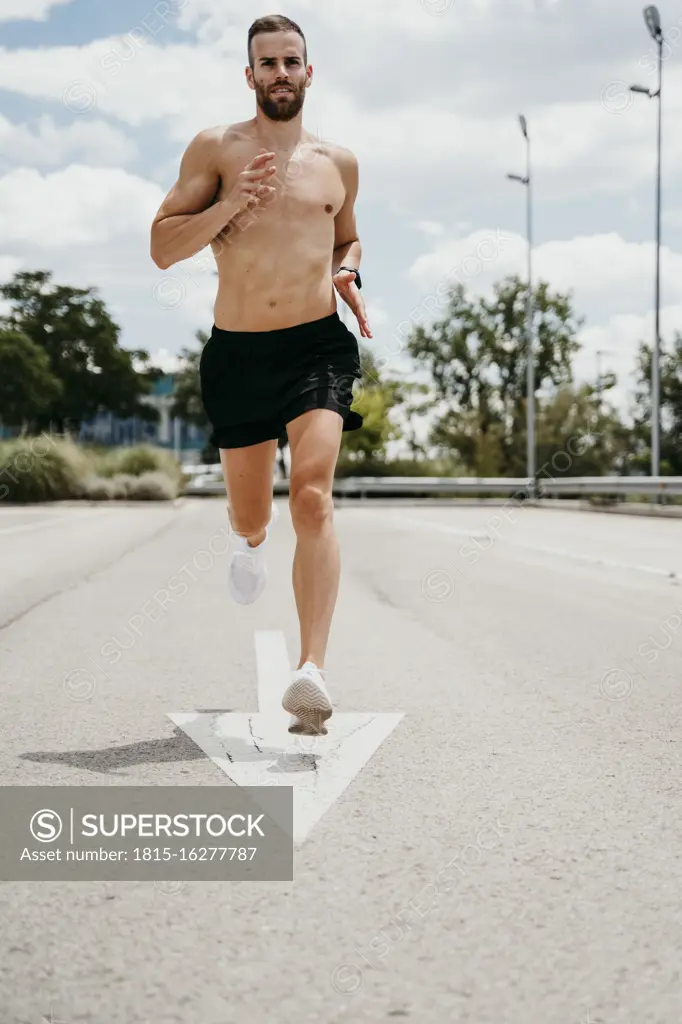 Barechested male athlete running with arrow sign on the road