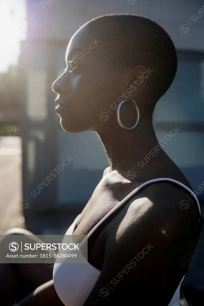 Close-up of thoughtful young woman with shaved head looking away while sitting outdoors during sunny day