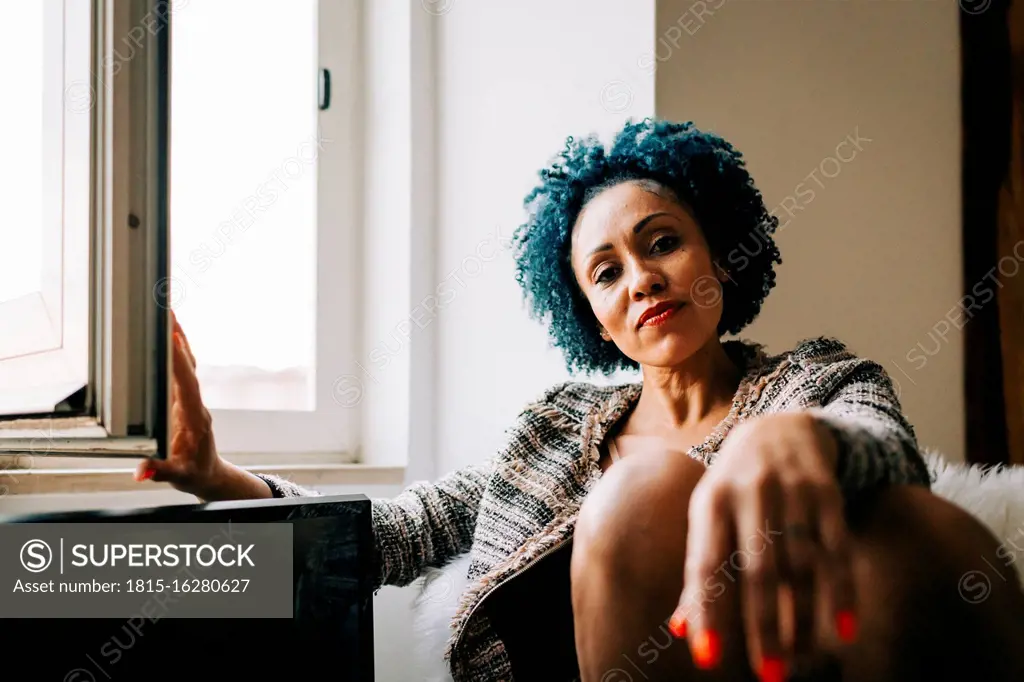 Mid adult woman with curly hair sitting by window at home