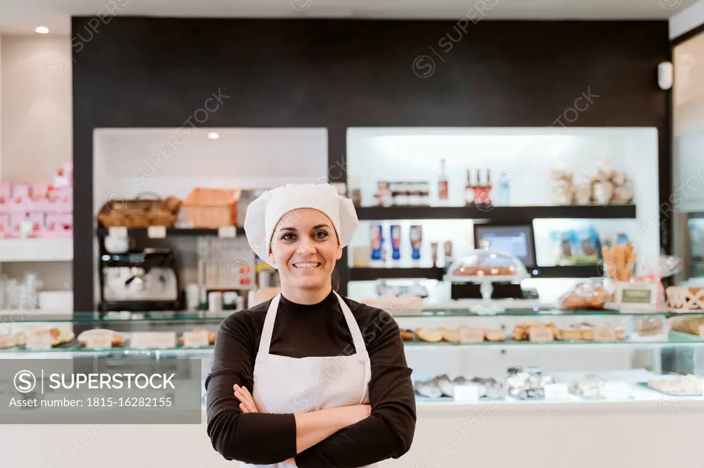 Happy female baker standing arms crossed at bakery