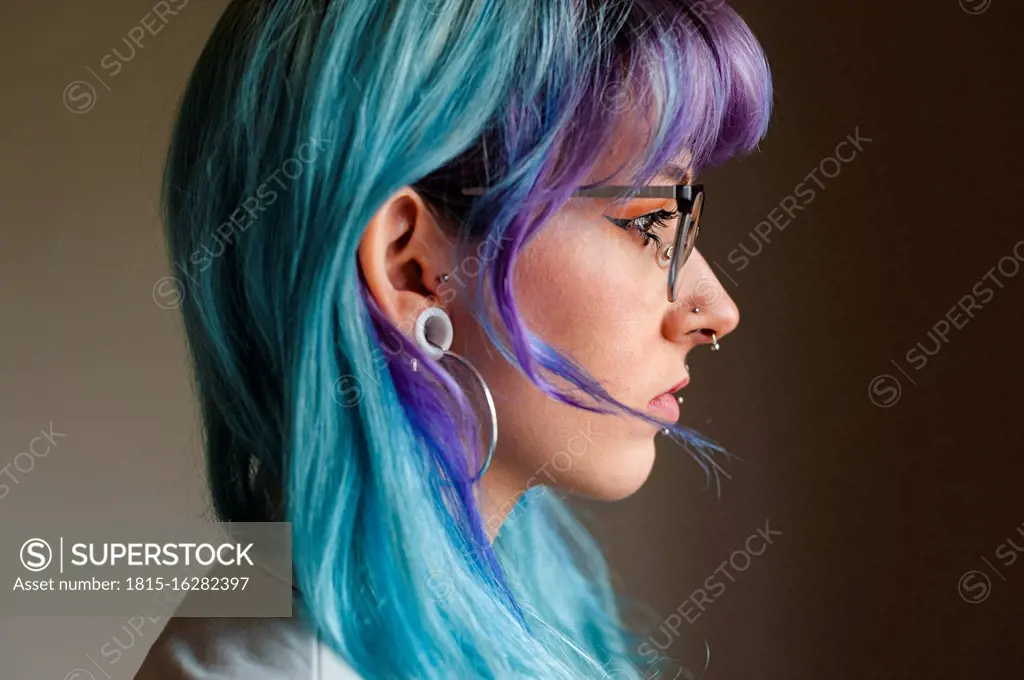 Close-up of thoughtful young woman with dyed hair and piercings against wall in old office