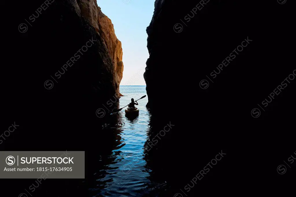 Woman kayaking in sea amidst mountains against clear sky