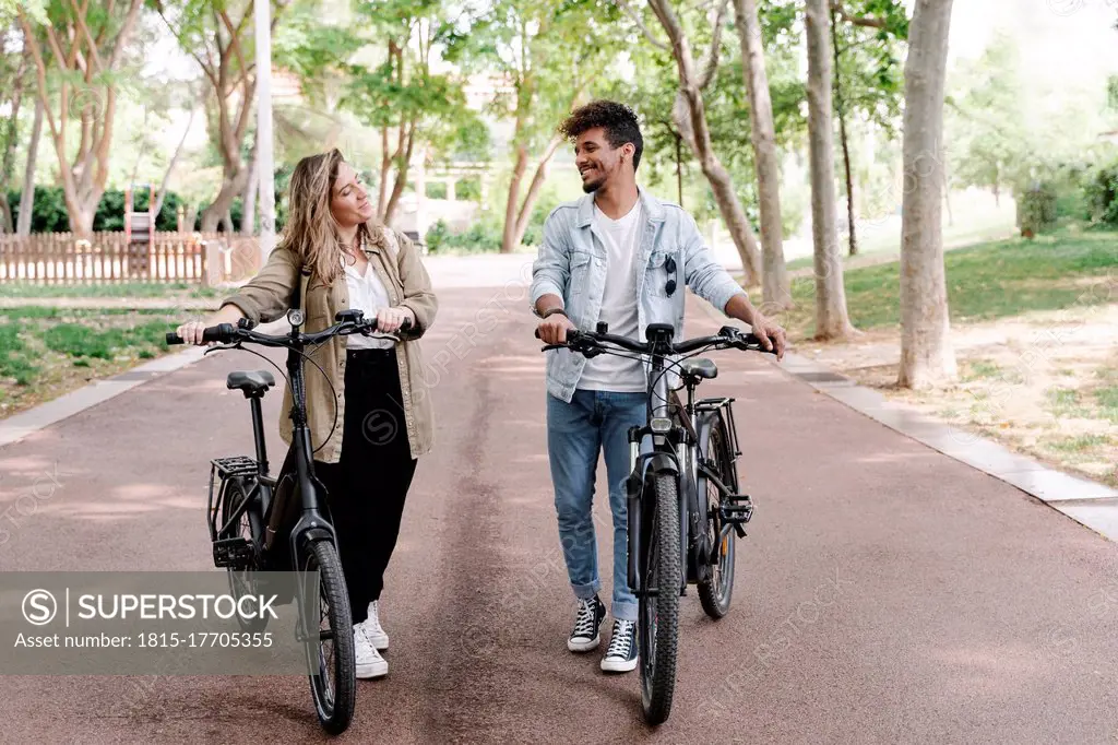 Smiling young couple with electric bicycles walking on road