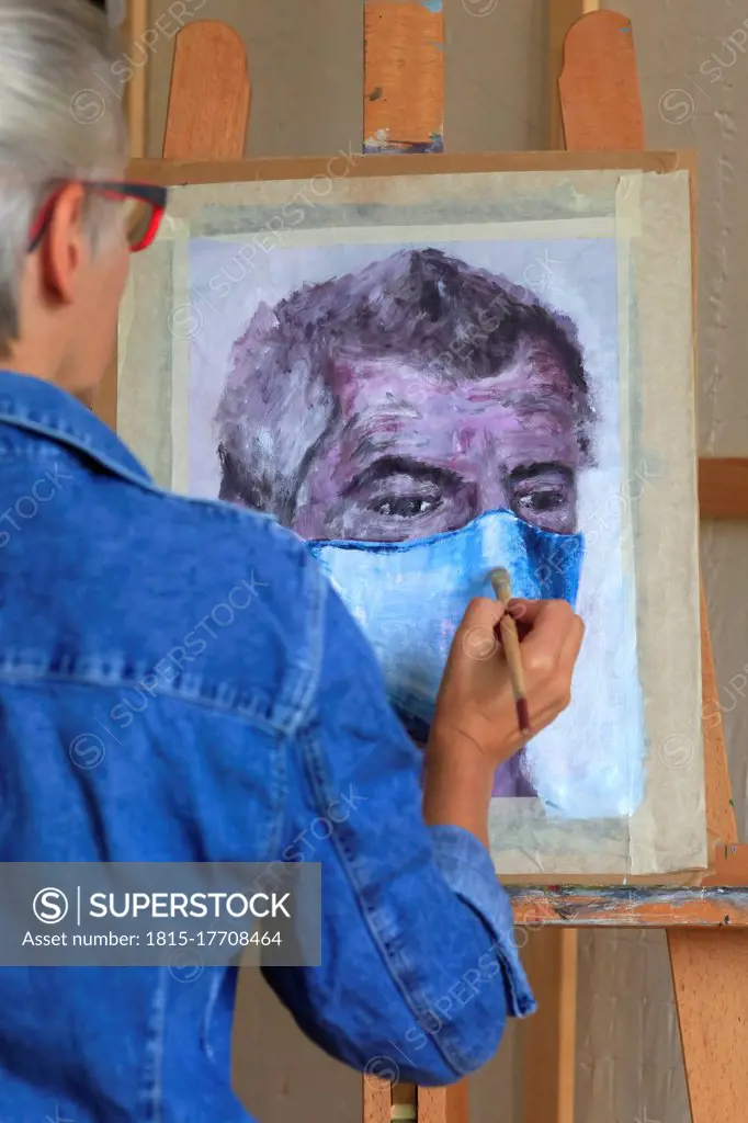 Woman painting man face with face mask on canvas at studio