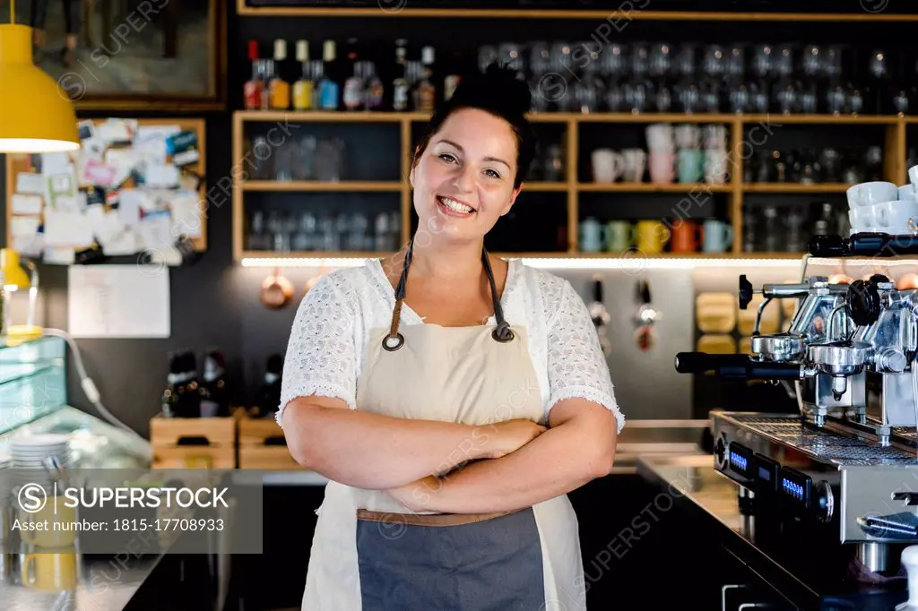 Smiling female barista with arms crossed standing in coffee shop