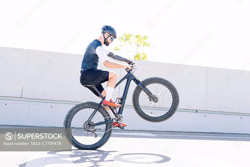 Male amputee athlete performing stunt with bicycle on road against clear sky