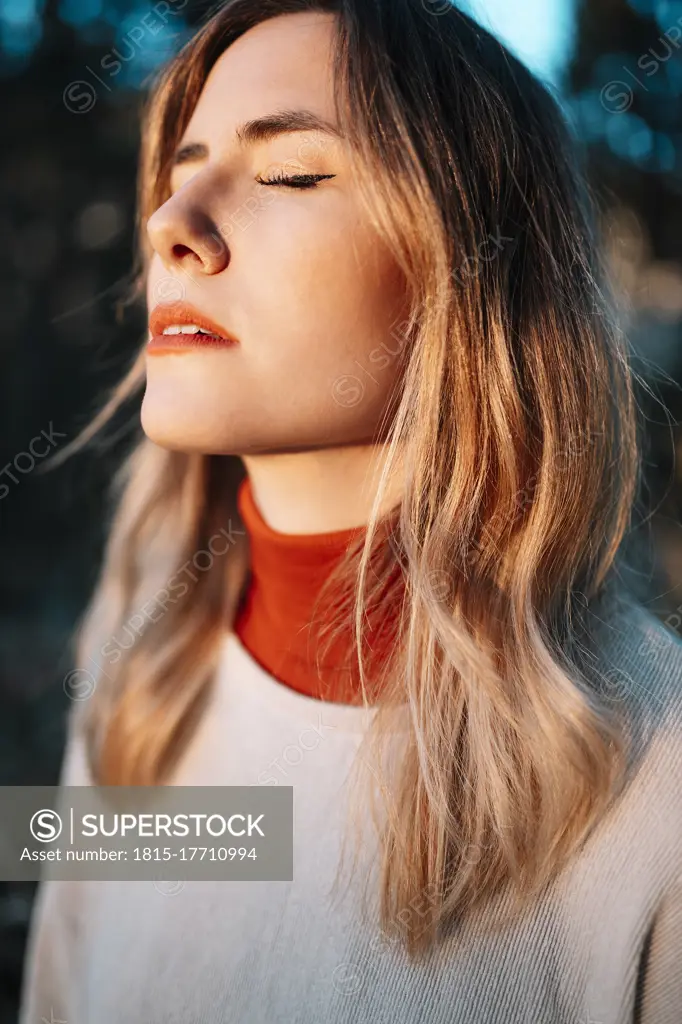Young woman standing with eyes closed during sunset