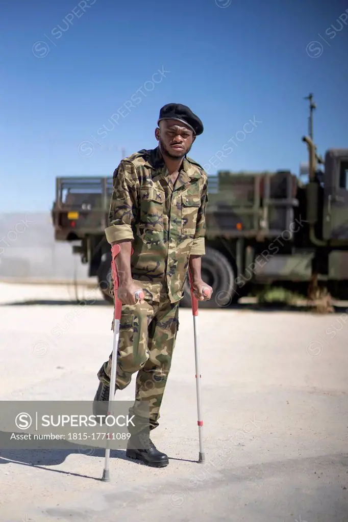 Injured army soldier standing with crutches on sunny day