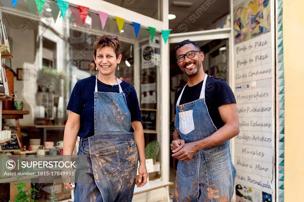Smiling coworkers wearing aprons standing outside ceramic shop