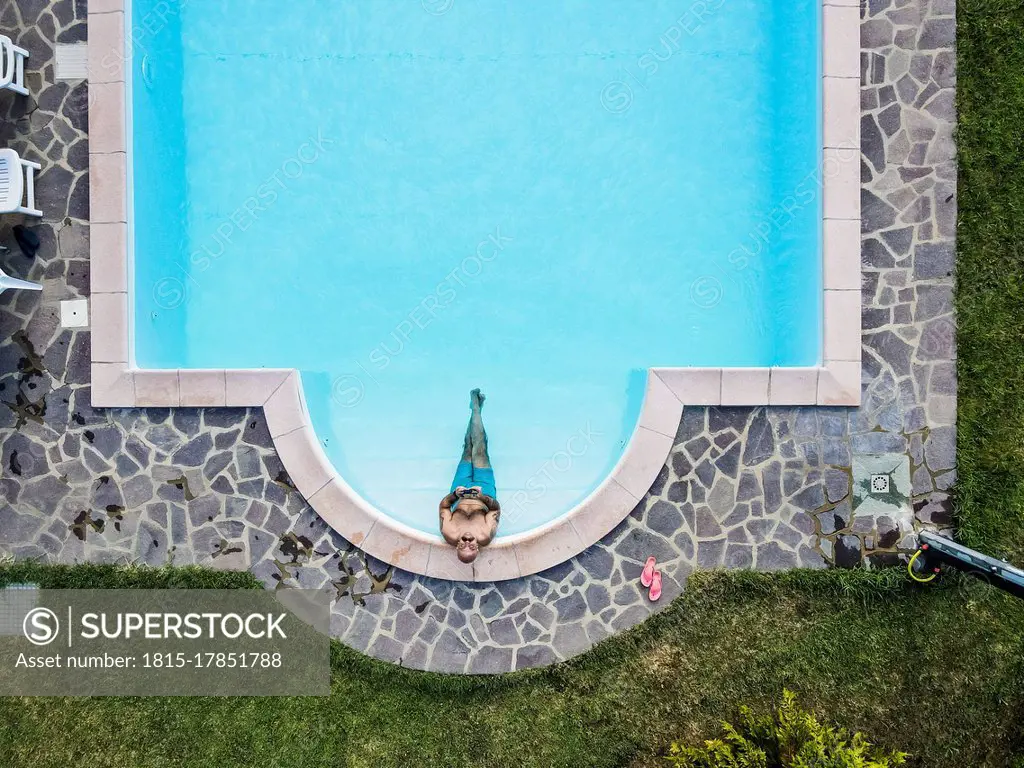 Drone view of man relaxing swimming pool