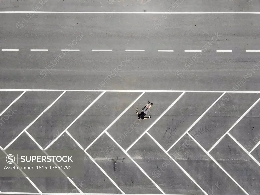 Drone view of man lying on back in empty parking lot
