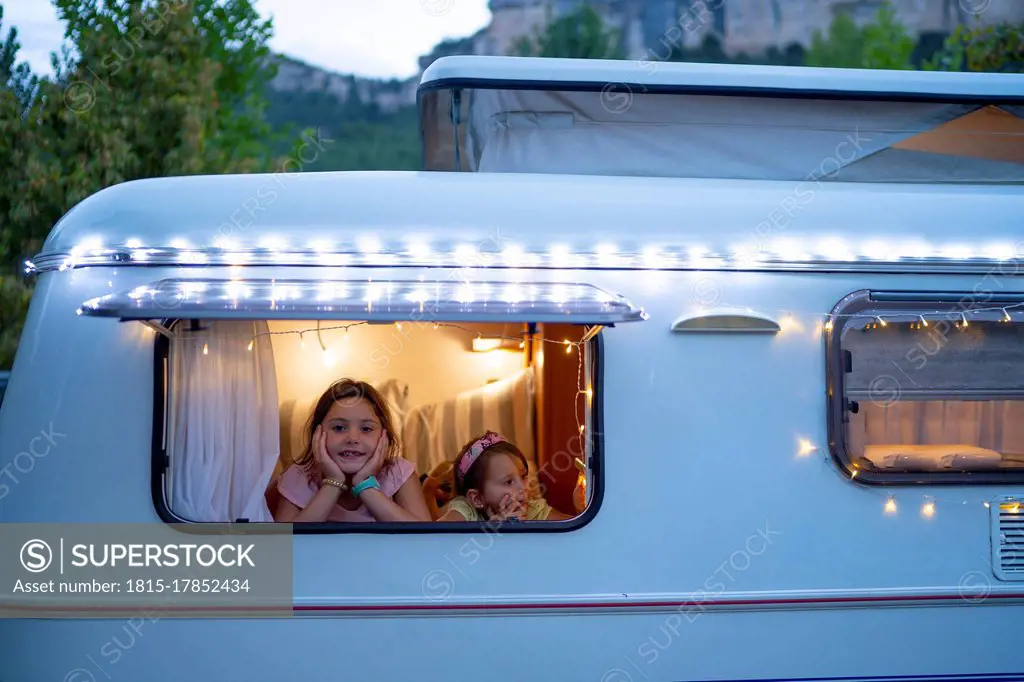 Sisters looking through window of illuminated motor home at dusk